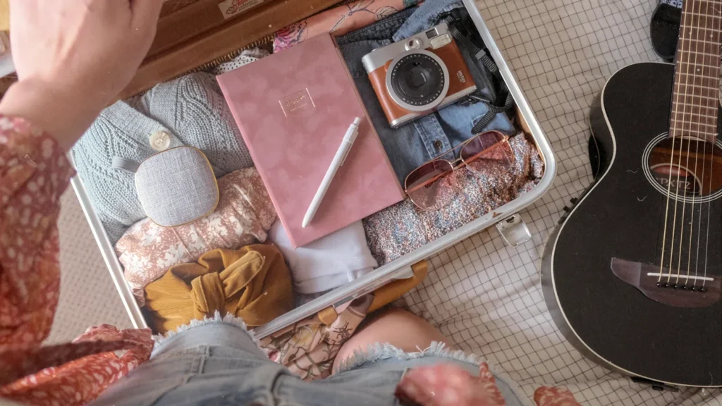 A person packing an open suitcase with clothes, a camera and travel essentials