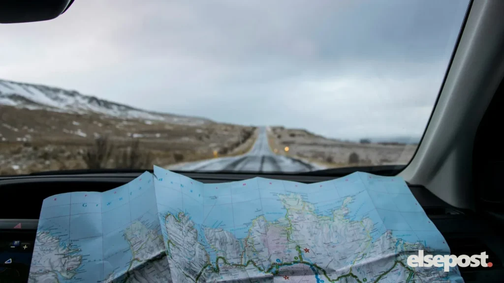 A paper map on a car dashboard facing an empty road through hills
