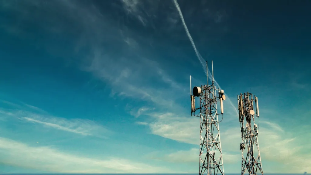Two telecom towers with antennas against a blue sky with thin clouds