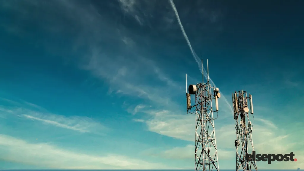 Two telecom towers with antennas against a blue sky with thin clouds