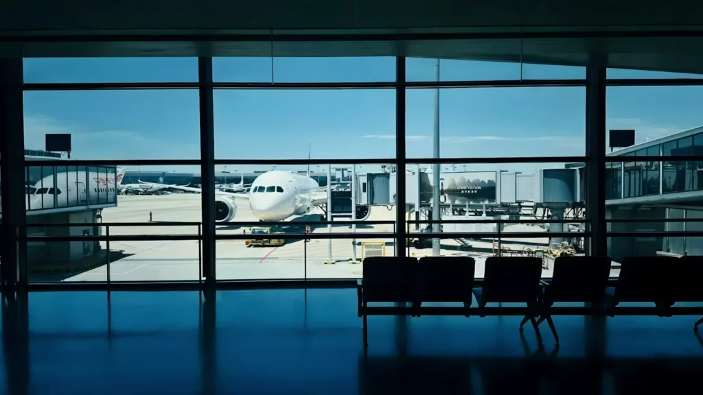An aircraft parked at an airport gate, seen through the tall windows of a quiet departure lounge