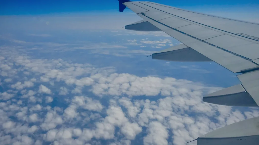 An aircraft wing above a layer of white clouds under a clear blue sky