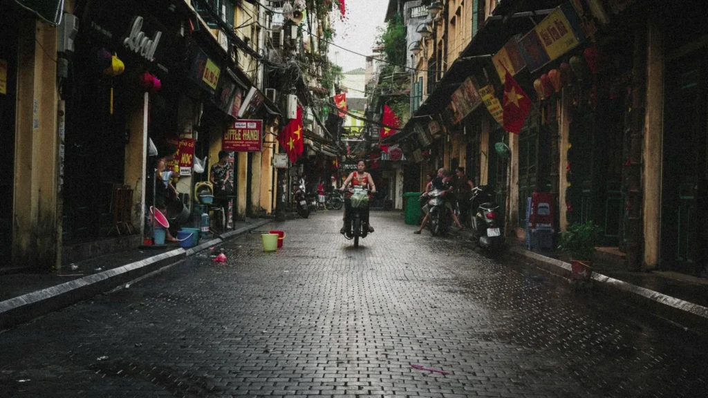 A narrow street lined with shops and flags in Hanoi Old Quarter, with a scooter in the distance