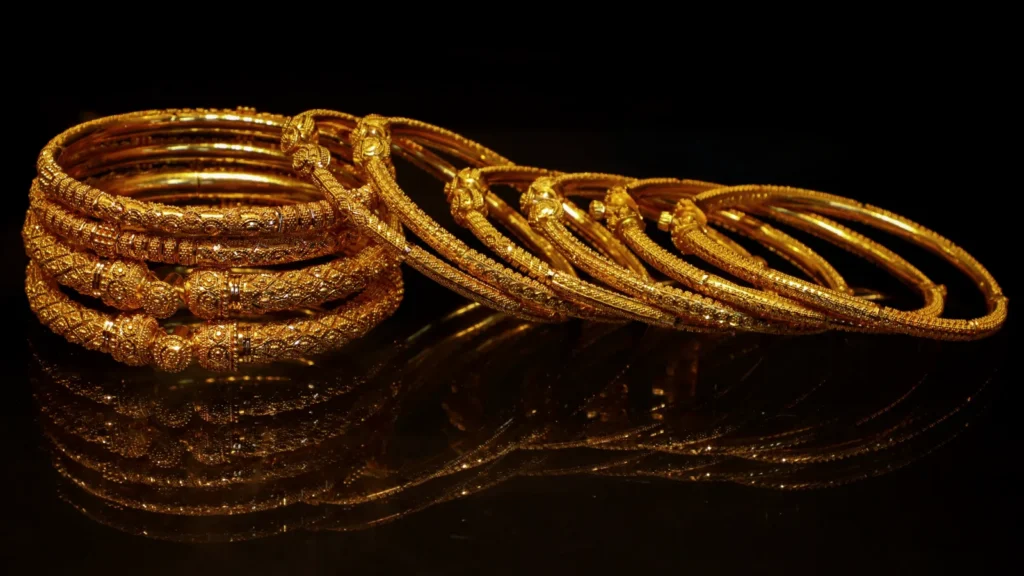 Stacked gold bangles with fine engraved patterns on a dark surface