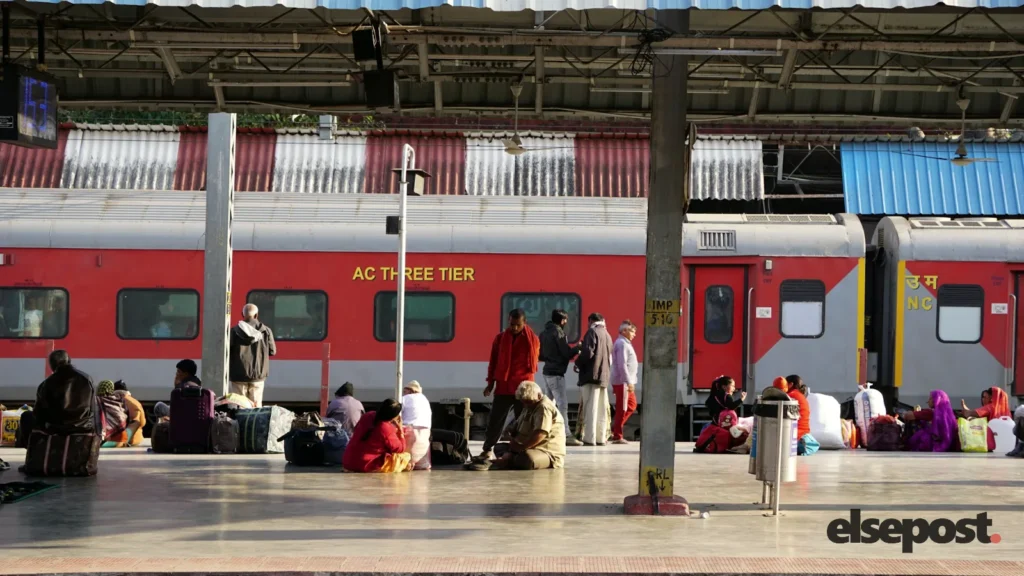 People standing on a railway platform next to a train for Tatkal ticket booking