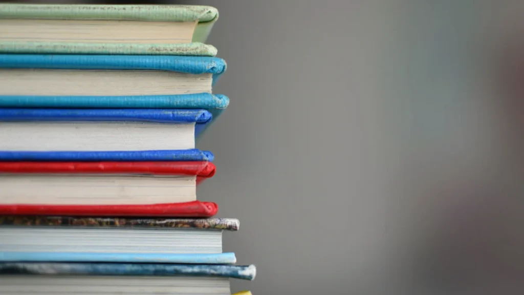 A close-up of a stack of hardback books with colourful spines against a soft grey background