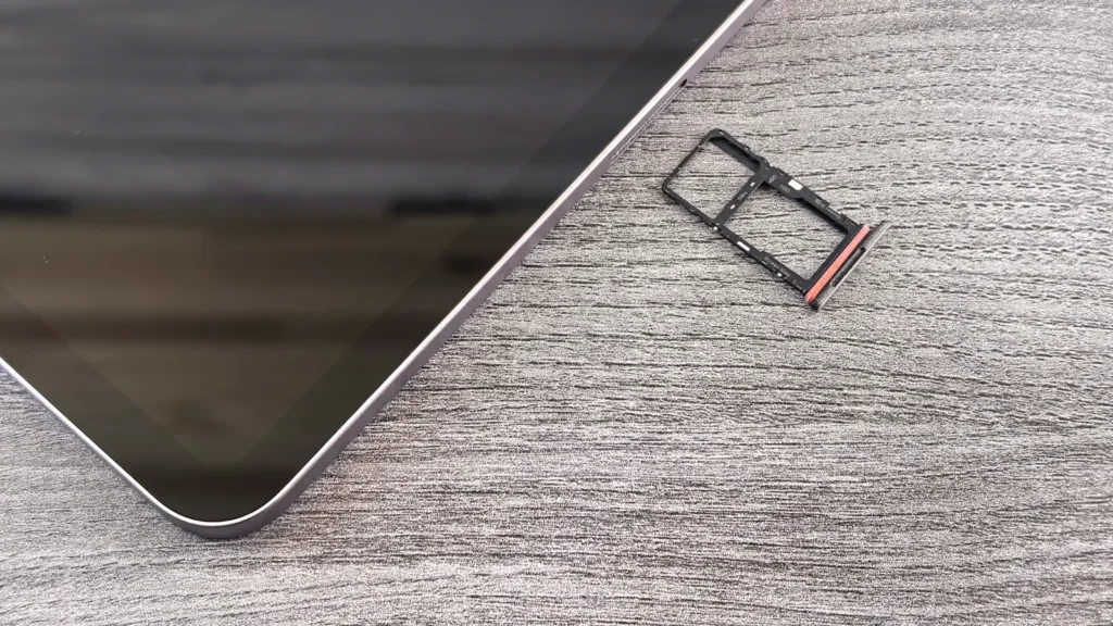 A smartphone lying on a grey wooden surface beside its removed SIM card tray