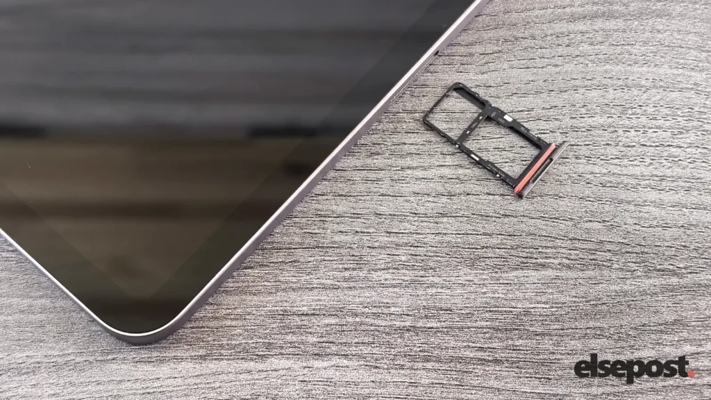 A smartphone lying on a grey wooden surface beside its removed SIM card tray