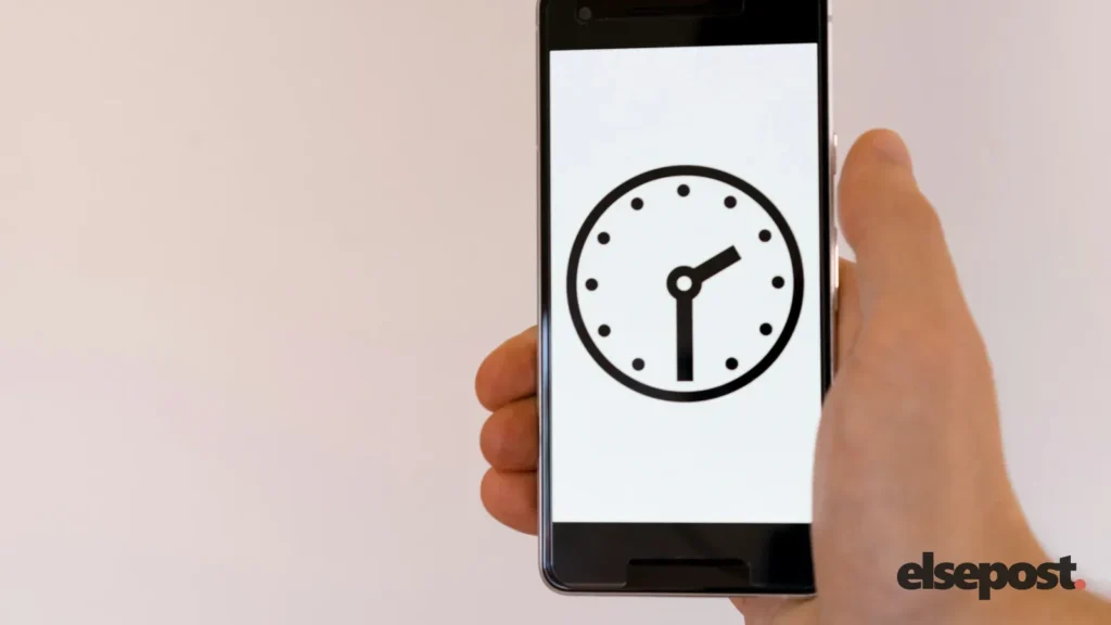 A hand holding a smartphone showing a clock face